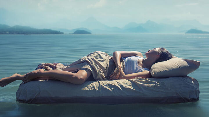 A woman sleeping on a mattress on a lake, mountains in the background